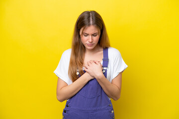 Young caucasian woman isolated on yellow background having a pain in the heart