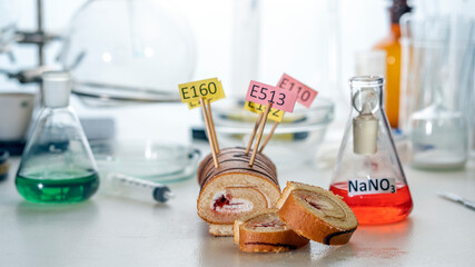 Food additives: sweet roll with chemical additives with colored labels, on a laboratory table....