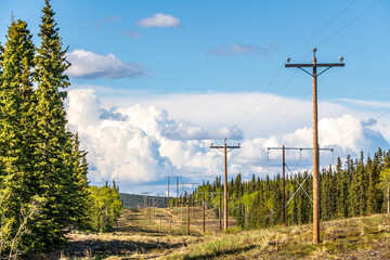 Electricity, power lines seen in rural Canada during summertime with blue sky, clouds and...