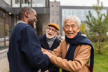 Senior asian man looking at camera near multiethnic friends on urban street.