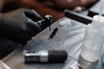 Professional male tattoo artist in black gloves makes ink and mixes paints using a mixer in the studio. Workspace of a tattoo artist. Tattoo preparation process