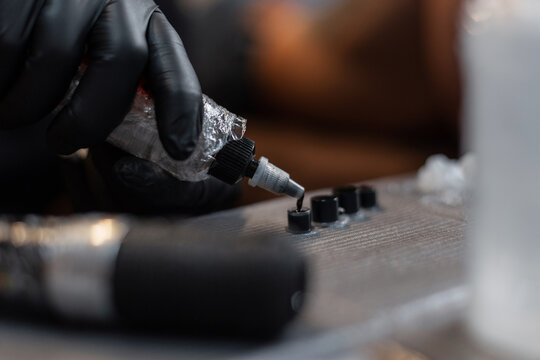 Professional man tattoo master prepares ink and spills paint on tubes, close-up. Work process
