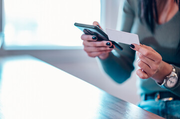Middle aged woman holding credit card and using smartphone at home