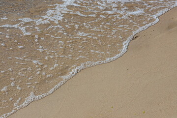 Close-up of sea foam on the sand beach with summer sunlight