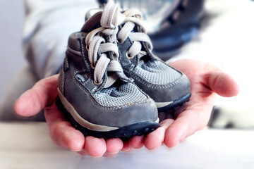 The family is waiting for replenishment: gray children's shoes are lovingly held by men's hands, close-up