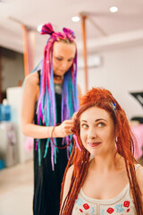 Hippie and boho style coiffure with kanekalon. Hairdresser with colored afro braids weaves to funny redhead girl ginger dreadlocks. Beauty salon services.