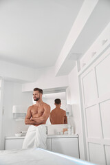 Cheerful man with bare chest leans onto cabinet in contemporary sap salon