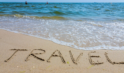 Travel concept - inscription in the sand. Sandy coast of the sea. Motivation. Ocean wave. The word travel is written on the sea beach. Vacations on the shore