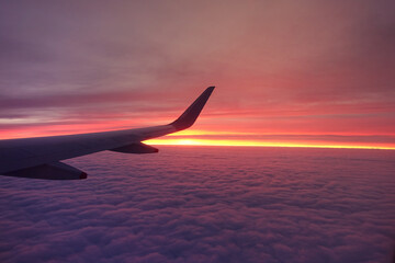 Sunset on cloudy sky as seen from a window plane above fluffy clouds