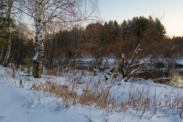 Winter landscape forest river with a bridge in the background at sunset.