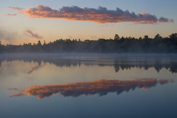 Fototapeta premium clouds reflecting on calm water morning mist hovering over lake at sunrise early morning fog or mist trees forest or woods reflecting in tranquil calming lake water blue sky purple clouds horizontal