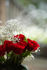 red roses and white tiny flowers in vase against glass of window valentines day or anniversary celebration love romance and  romantic mood vertical format with room for type symbolizing relationship 