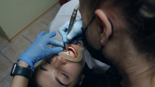A woman dentist works with a patient in the dentist's office, top view. A patient with a cheek retractor in his mouth in a modern dental clinic