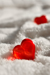 Close up red glass heart on white fur background. Minimalist greeting mock concept for Valentines day, Mothers day, romantic data or wedding. Trendy sunlight still life. Vertical shot.