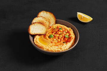 An appetizer Hummus served with fresh pita bread and herbs, seasoned with extra virgin olive oil and paprika in vintage ceramic plate on the dark background