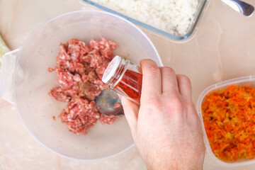 A man spices smoked paprika into minced meat in a bowl for lazy cabbage rolls on the table.