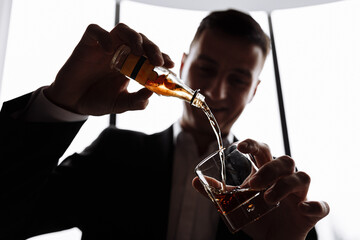 smiling male businessman in suit pours a glass of alcohol, cognac or whiskey, from a mini bottle in the hotel
