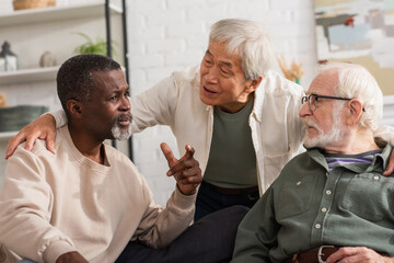 Elderly interracial friends talking in living room.