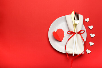Composition for Valentine's Day February 14. Festive dinner. A plate with a fork and hearts cut out of paper on a red background. Flat lay, top view, copy space.