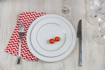 Serving plate, spoon, fork, knife and red napkin are on the wooden table. The concept of weight loss and diet. Tomatoes on two large plates
