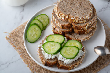 Slices of rye bread with cottage cheese and cucumbers on white background