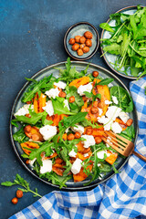 Summer salad with grilled peach with soft cheese, hazelnuts and arugula on blue table background, top view, copy space