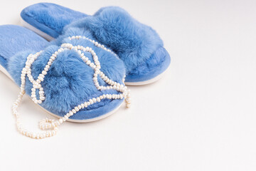 Fototapeta na wymiar Blue women's home slippers and pearl necklace. Comfortable shoes for home. Space for text
