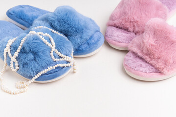 Fototapeta na wymiar Blue and pink women's home slippers and pearl necklace. Comfortable shoes for home. Space for text