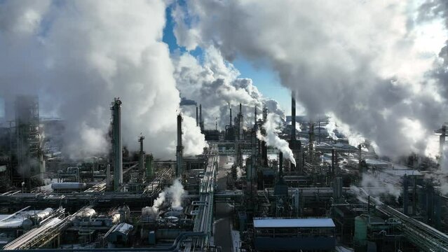 Smoke billowing from oil refinery plant on winter day. Stock drone footage with camera zooming out above petrochemical processing complex.