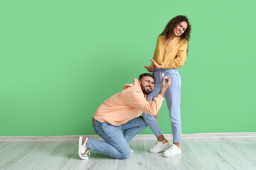 Young African-American woman rejecting marriage proposal of her begging boyfriend on color background