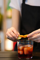 Bartender decorating glass of tasty Negroni cocktail at table in bar