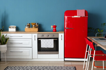 Interior of stylish kitchen with red fridge, white counters and blue wall