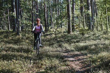 Obraz premium Active woman cycling on forest road. Female riding bicycle off-road route on summer vacation day. Woman wearing bicycle helmet and gloves