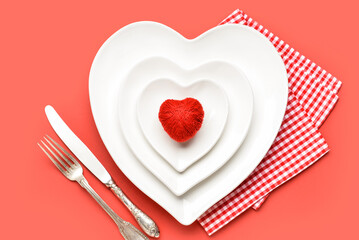 Beautiful heart-shaped plates and cutlery on red background