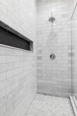 A large luxury shower with marble subway tile walls, marble hexagon floor, and black hexagon tiled shelf.