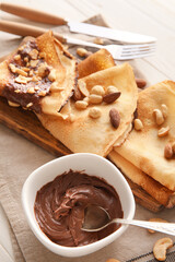 Board of tasty thin pancakes with chocolate paste and nuts on table