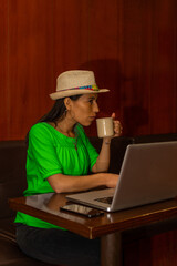 Young latin woman working on her laptop while drinking a cup of coffee