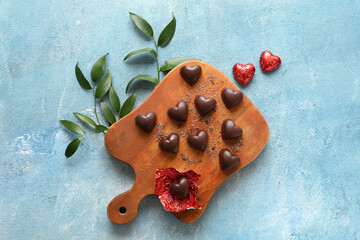 Board with tasty heart-shaped candies on color background
