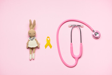Obraz na płótnie Canvas Golden awareness ribbon, toy rabbit and stethoscope on color background. International Childhood Cancer Day
