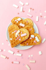 Homemade Belgian waffles heart shaped on plate with colorful sweet mini confetti, sprinkles, marsmallow dessert food. pink background for Valentines day, womens day, love, romance, party pattern