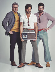 Ready to kick it retro style. A studio shot of three men clad in retro 70s wear holding a cassette...