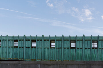 Part of elevated station in Boston. Green metal wall exterior of a train platform