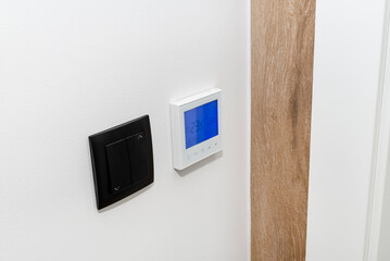 A wall-mounted room thermostat showing a temperature of 23.5 degrees Celsius, next to it a black switch for roller blinds.