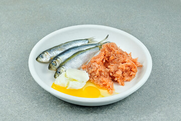 Natural raw cat food in bowl on grey background Fish, minced fish, eggs and yoghurt