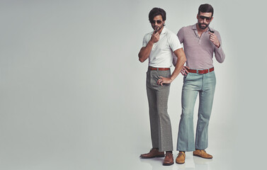 They've got far out style. Studio shot of two men standing together while wearing retro 70s wear and smoking pipes.