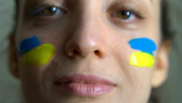 Young girl is paining blue and yellow ukrainian flag on her cheek using her fingers wearing military uniform, mandatory conscription in Ukraine, equality concepts
