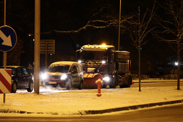 Pojazdy pług i piaskarka na drodze po nocnych opadach śniegu w mieście i ruch pojazdów.  - obrazy, fototapety, plakaty