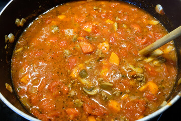 Simmering pot of homemade tomato pasta sauce stirred with wooden spoon