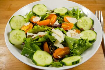 Fresh Salad with parmasan cheese shavings on bed of spring mix lettuce with cucumber and yellow tomatoes
