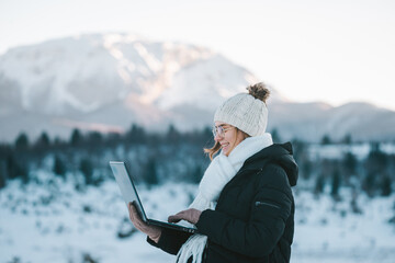 young smiling woman freelancer using laptop outdoors in snow mountains - obrazy, fototapety, plakaty